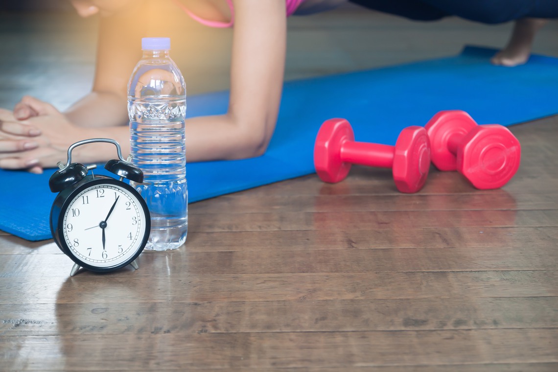 Alarm clock, bottle of water, dumbbells and asian woman yoga at home in background, Working out and lifestyle concept, Selective focus