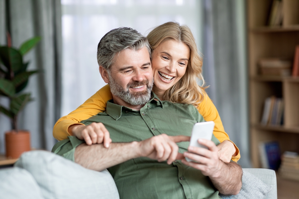 Happy,Middle,Aged,Couple,Using,Mobile,Phone,At,Home,Together,