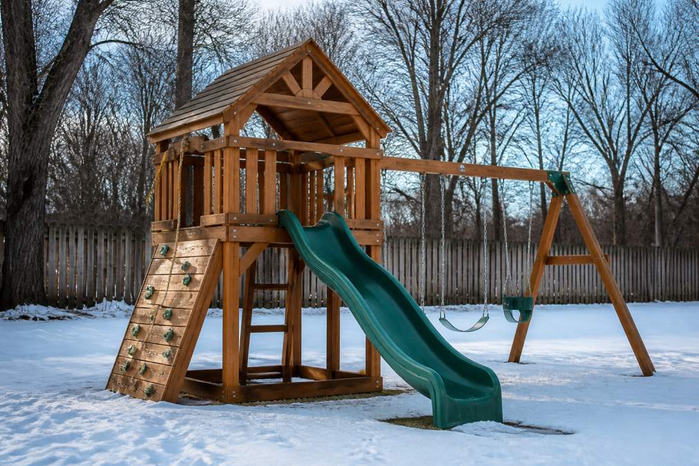 A sturdy wooden playset standing in a Pennsylvania backyard during winter, showing quality craftsmanship with reinforced joints, proper finishing, and stability against snow-covered ground and bare trees